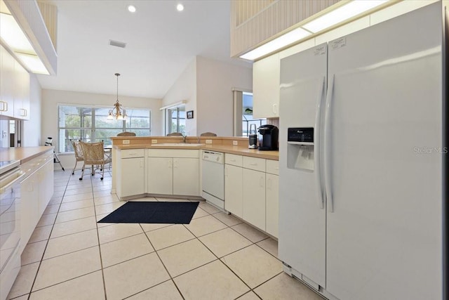 kitchen with a sink, white appliances, a peninsula, light countertops, and light tile patterned floors