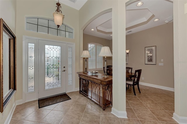 foyer entrance with ornamental molding, a tray ceiling, and light tile patterned floors