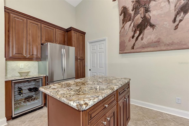 kitchen featuring a kitchen island, stainless steel refrigerator, tasteful backsplash, beverage cooler, and light stone countertops