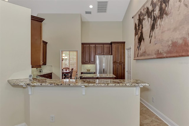 kitchen with light stone countertops, light tile patterned floors, stainless steel fridge, and kitchen peninsula