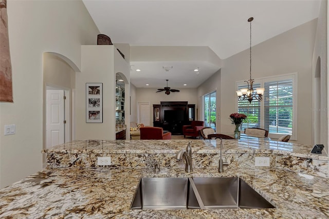 kitchen featuring sink, ceiling fan with notable chandelier, light stone counters, and decorative light fixtures