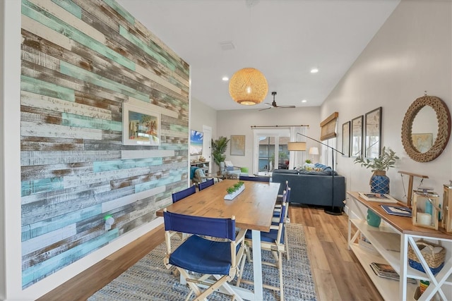 dining space with ceiling fan, a barn door, wooden walls, and light hardwood / wood-style floors