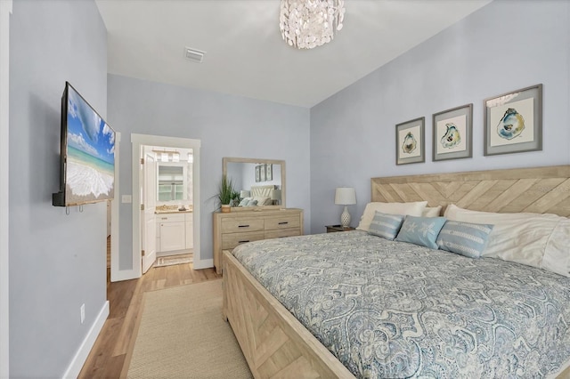 bedroom with ensuite bathroom, a chandelier, and light hardwood / wood-style floors