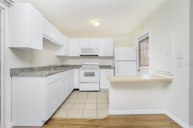 kitchen featuring white appliances, light wood finished floors, white cabinets, a peninsula, and a sink