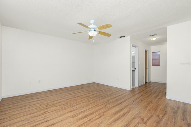 empty room featuring a textured ceiling, ceiling fan, baseboards, and light wood-style floors