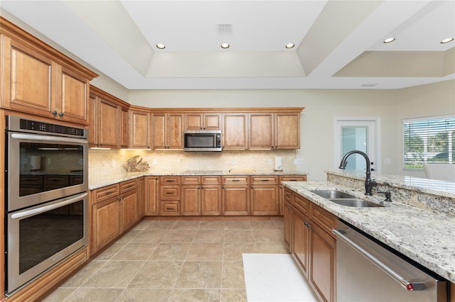 kitchen with light stone counters, stainless steel appliances, a tray ceiling, and sink