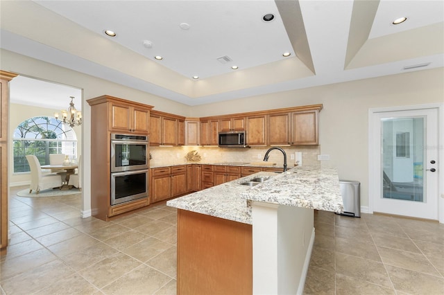 kitchen featuring a raised ceiling, sink, kitchen peninsula, stainless steel appliances, and light stone countertops