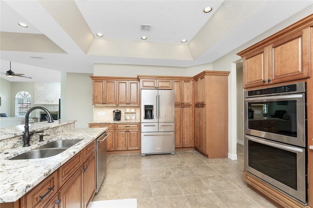 kitchen featuring light stone countertops, appliances with stainless steel finishes, sink, and a tray ceiling