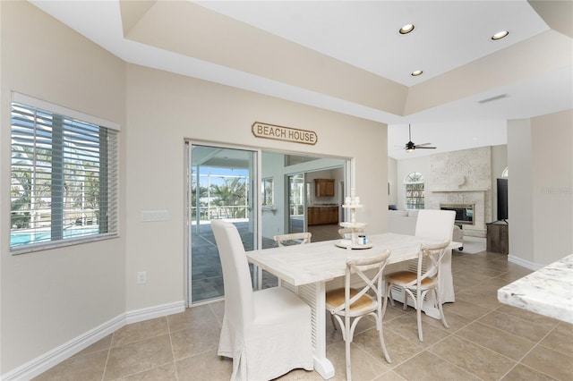 dining area with light tile patterned floors, a tray ceiling, a fireplace, and ceiling fan