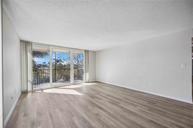 spare room featuring a textured ceiling, a wall of windows, and light hardwood / wood-style flooring