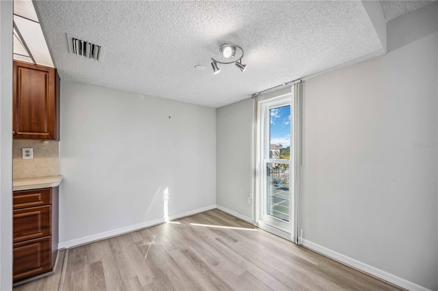 unfurnished dining area featuring a textured ceiling and light wood-type flooring