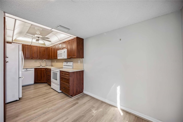 kitchen featuring sink, white appliances, a textured ceiling, and light wood-type flooring