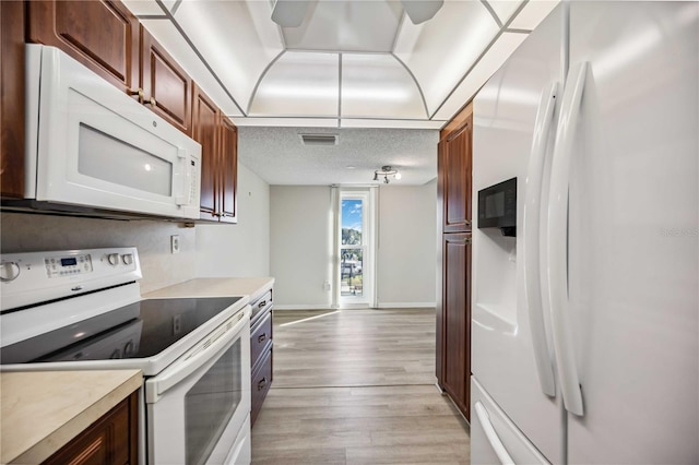 kitchen with a textured ceiling, white appliances, and light hardwood / wood-style flooring