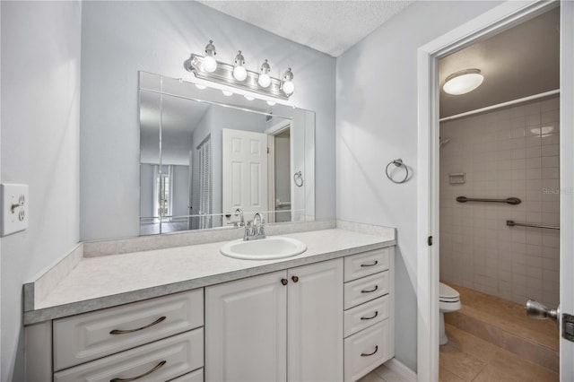 bathroom with vanity, tiled shower, a textured ceiling, and toilet