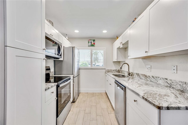 kitchen with stainless steel appliances, light stone countertops, sink, and white cabinets