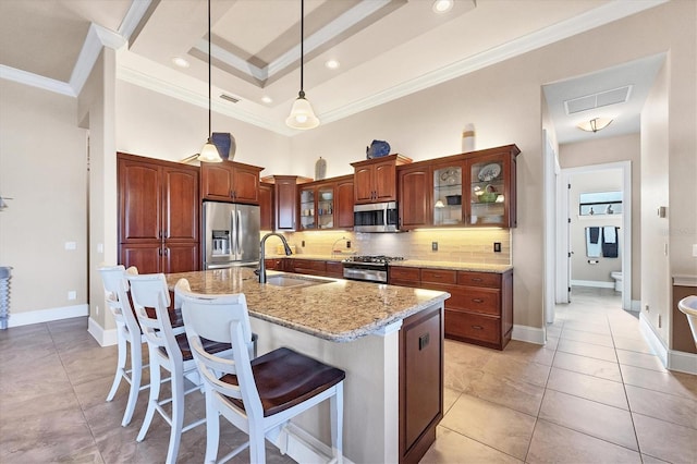 kitchen featuring appliances with stainless steel finishes, an island with sink, sink, hanging light fixtures, and a tray ceiling