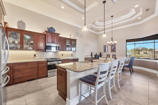 kitchen featuring sink, appliances with stainless steel finishes, hanging light fixtures, light stone counters, and a raised ceiling