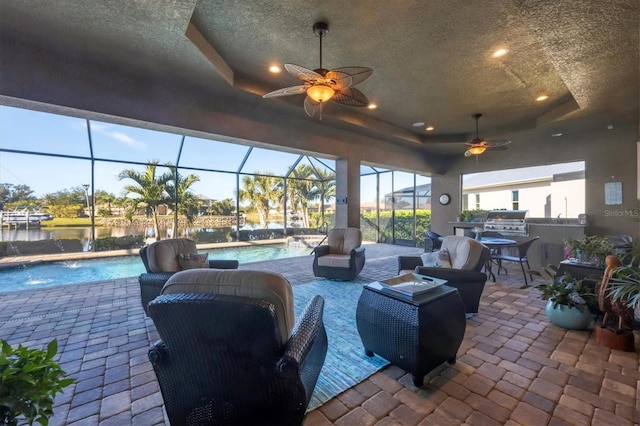 view of patio with an outdoor kitchen, pool water feature, a lanai, ceiling fan, and a water view