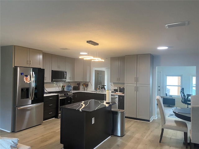 kitchen featuring stainless steel appliances, a center island, pendant lighting, and light hardwood / wood-style flooring