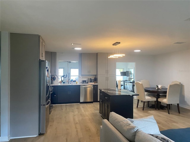 kitchen with sink, light hardwood / wood-style flooring, appliances with stainless steel finishes, a kitchen island, and decorative light fixtures