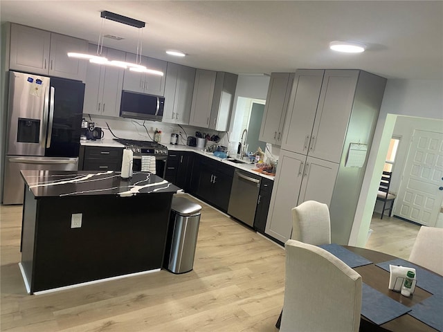 kitchen featuring sink, hanging light fixtures, stainless steel appliances, a center island, and light wood-type flooring