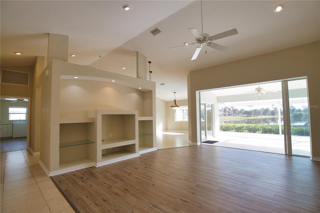 unfurnished living room featuring hardwood / wood-style flooring, built in features, ceiling fan, and a towering ceiling