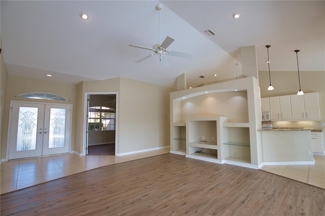 unfurnished living room featuring french doors, built in shelves, high vaulted ceiling, light wood-type flooring, and ceiling fan