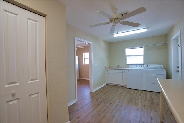 laundry area featuring washer and dryer, sink, cabinets, light hardwood / wood-style floors, and a healthy amount of sunlight