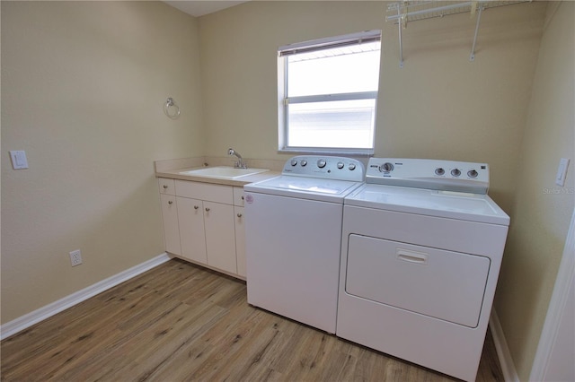 clothes washing area featuring cabinets, sink, washing machine and dryer, and light wood-type flooring