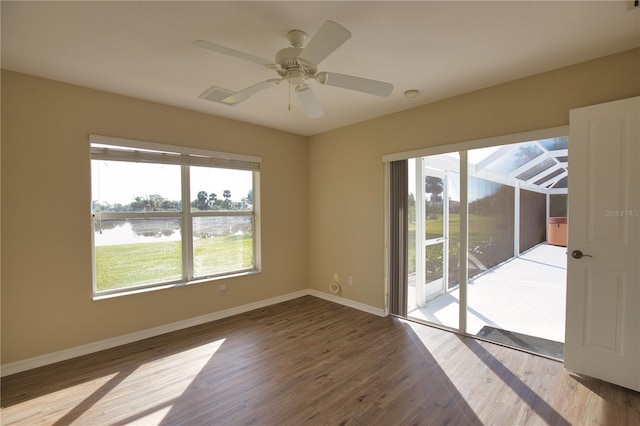 empty room featuring a water view, ceiling fan, and hardwood / wood-style floors