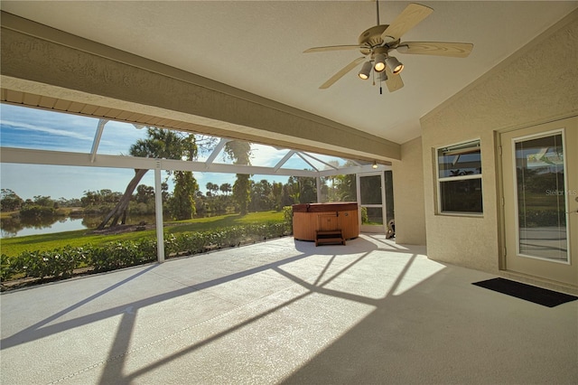 view of patio / terrace featuring a water view, ceiling fan, a hot tub, and glass enclosure