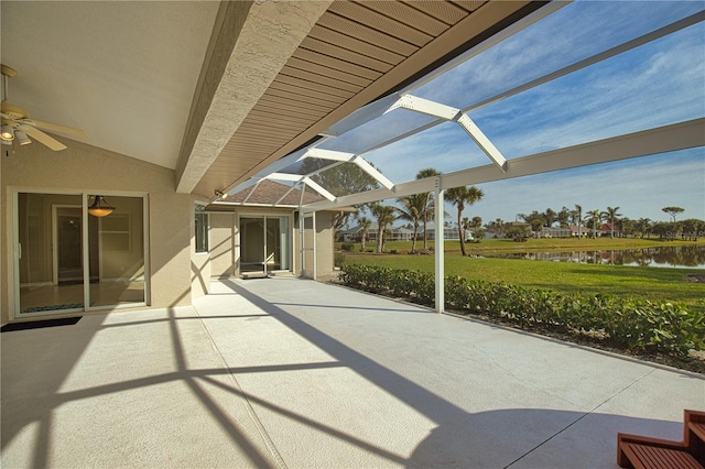 view of patio with ceiling fan, a water view, and glass enclosure