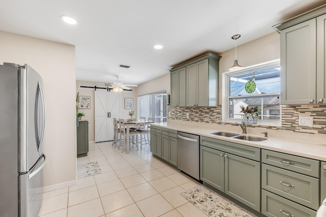 kitchen with sink, hanging light fixtures, appliances with stainless steel finishes, a wealth of natural light, and a barn door