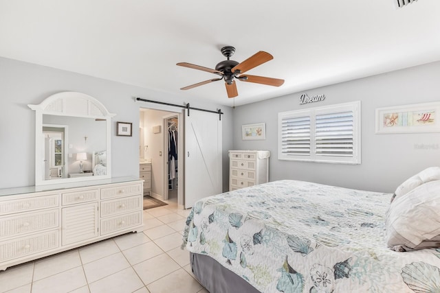 tiled bedroom featuring a barn door, ceiling fan, and ensuite bathroom