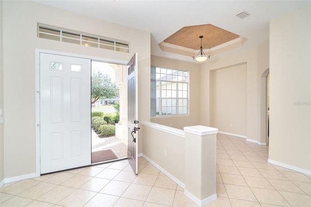 entrance foyer with a raised ceiling, light tile patterned flooring, arched walkways, and visible vents