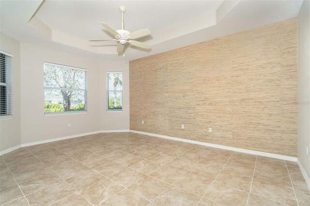 empty room with light tile patterned floors, a tray ceiling, and ceiling fan