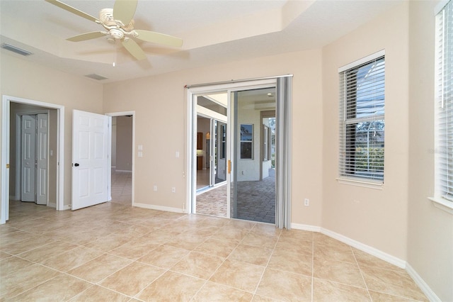 unfurnished bedroom with light tile patterned floors, visible vents, baseboards, a tray ceiling, and access to exterior