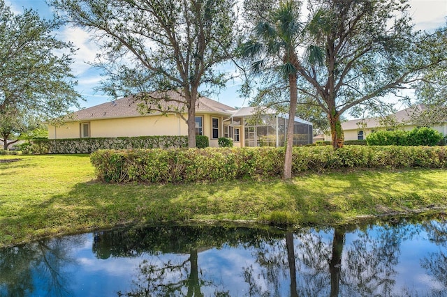 back of property with a water view, glass enclosure, and a lawn