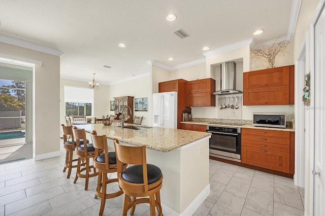 kitchen featuring wall chimney range hood, sink, a kitchen island with sink, stainless steel appliances, and a kitchen bar