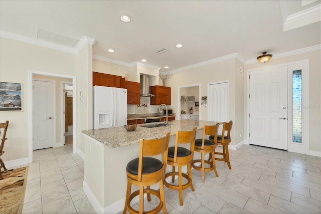 kitchen with a breakfast bar, sink, wall chimney range hood, white fridge with ice dispenser, and a center island with sink