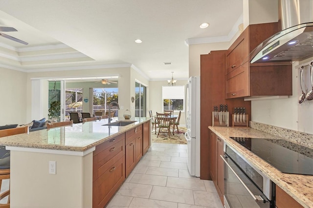 kitchen featuring sink, a kitchen island with sink, ventilation hood, light stone countertops, and ceiling fan with notable chandelier