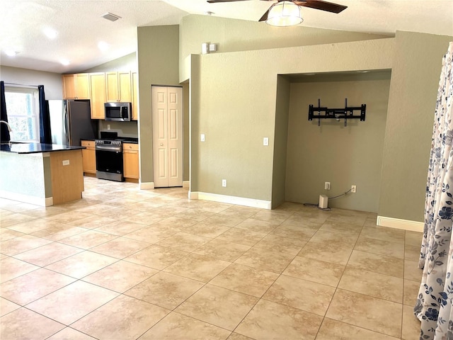 kitchen with light brown cabinetry, vaulted ceiling, light tile patterned floors, ceiling fan, and stainless steel appliances