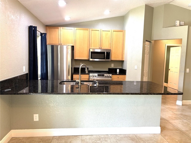 kitchen with lofted ceiling, appliances with stainless steel finishes, kitchen peninsula, and dark stone countertops