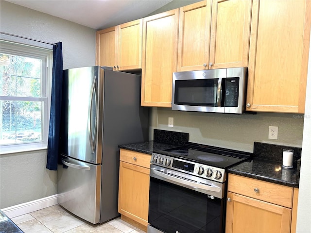 kitchen with appliances with stainless steel finishes, dark stone countertops, and light brown cabinetry