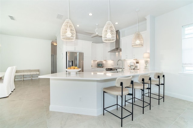 kitchen with stainless steel refrigerator with ice dispenser, white cabinets, pendant lighting, and wall chimney range hood