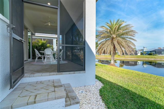 entrance to property featuring a water view, ceiling fan, a yard, and a patio area