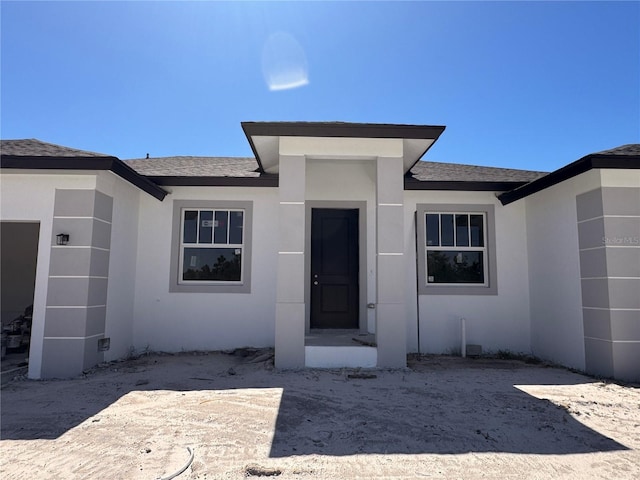 entrance to property featuring stucco siding and roof with shingles