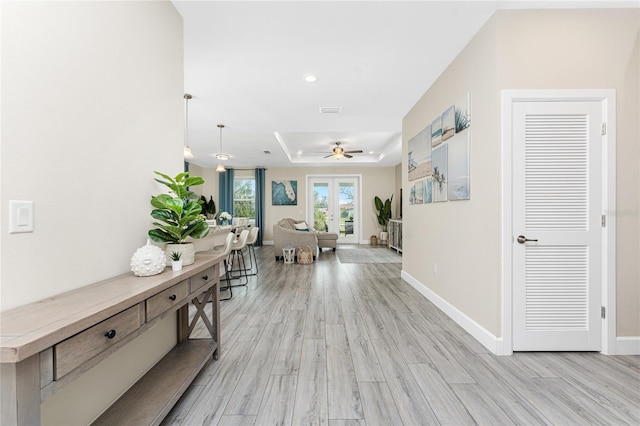 corridor featuring light wood-type flooring and a tray ceiling