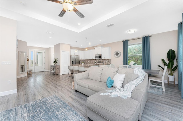 living room featuring a raised ceiling, ceiling fan, and light wood-type flooring