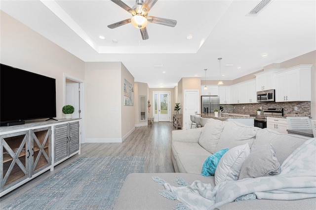 living room with a raised ceiling, ceiling fan, and light hardwood / wood-style floors